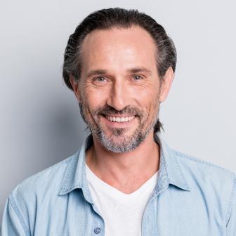 Mittelalterlicher Mann mit grauem Bart und zurückgekämmten Haaren lächelt freundlich in die Kamera